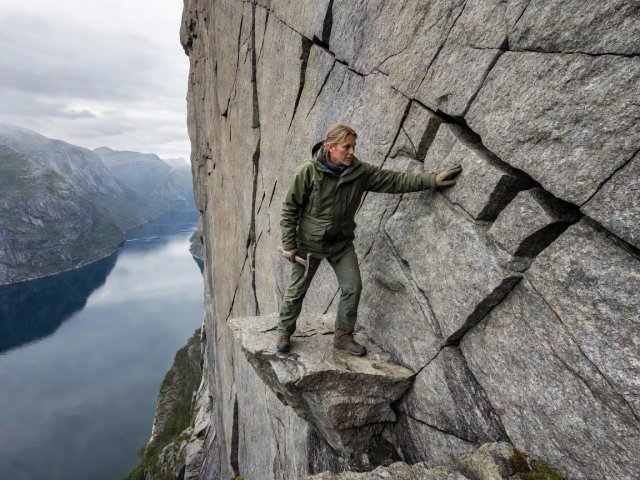 Walker examining right-angle tectonic joint fractures on a granitic gneiss cliff ledge above a Norwegian fjord